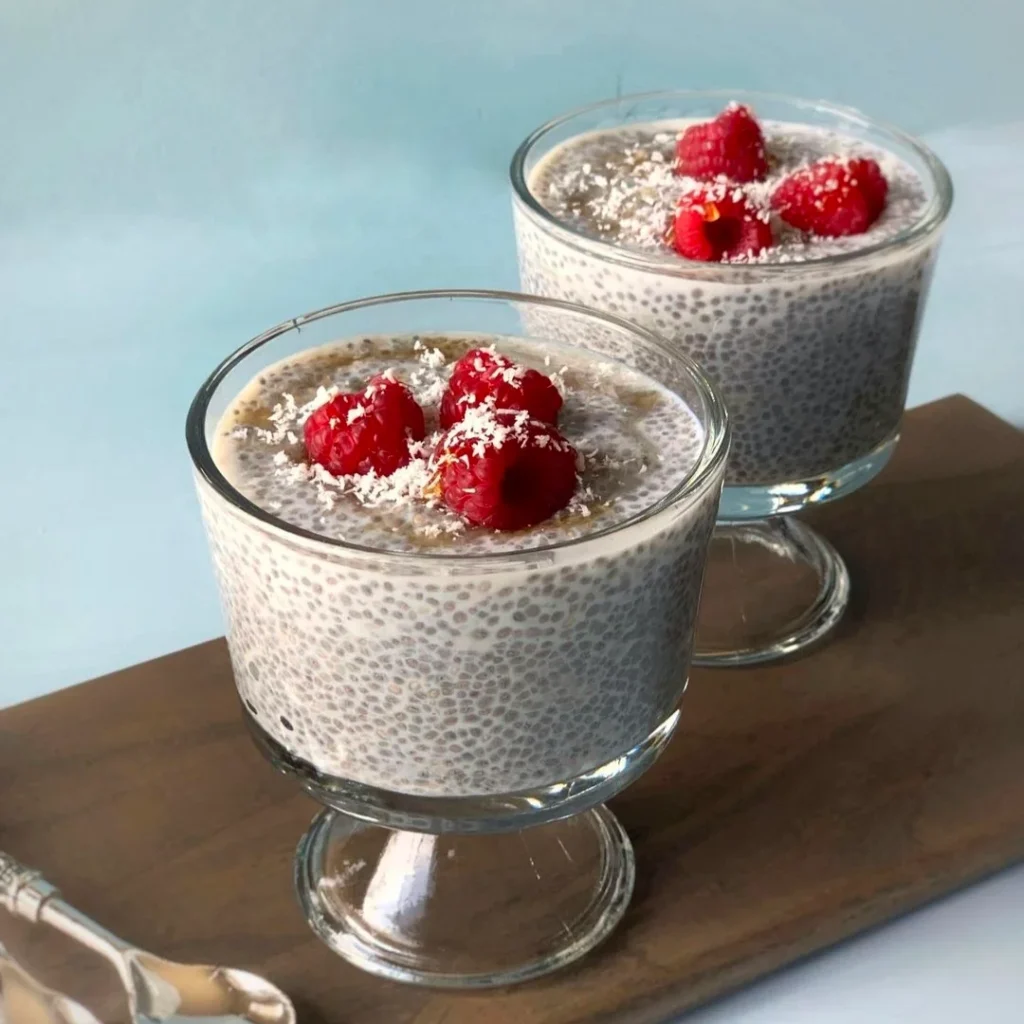 Two serving cups of chia puddings and red berries on the wooden tray.