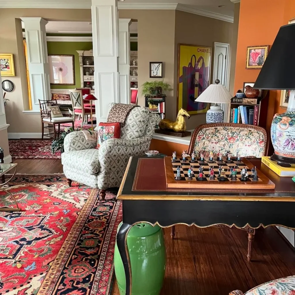 A well-decorated granny chic living room with lots of lamps, antique pieces, sofas, chess on the table, and wall hangings is shown.