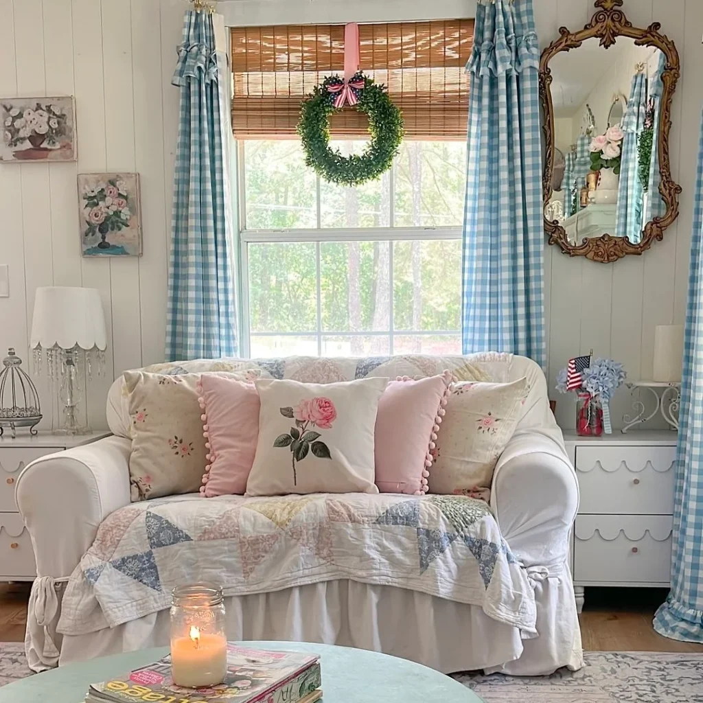 A sweet granny chic living room having a whit sofa with cushions, side drawer tables, hanging mirrors, wall pictures and window hangings.