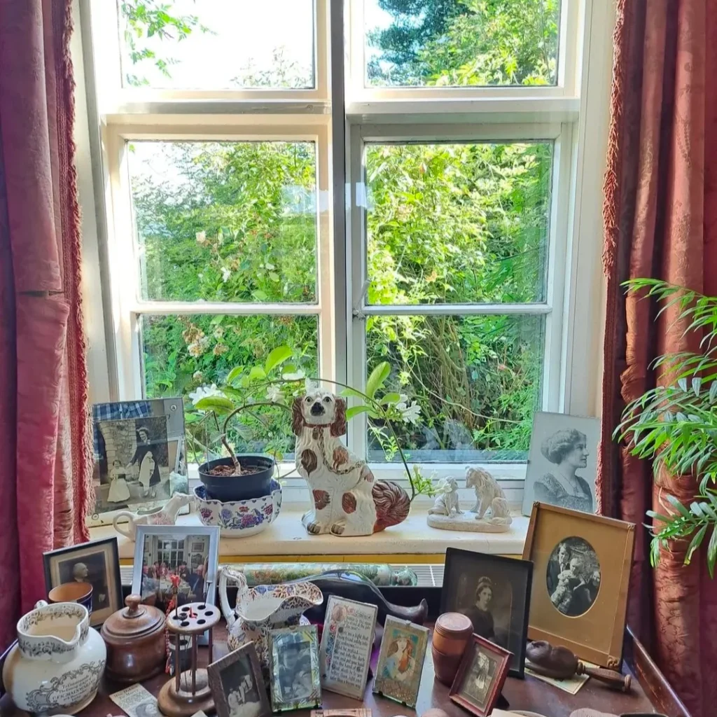 Vintage framed pictures and traditional pieces are placed on the window and on the table in front of the open window.