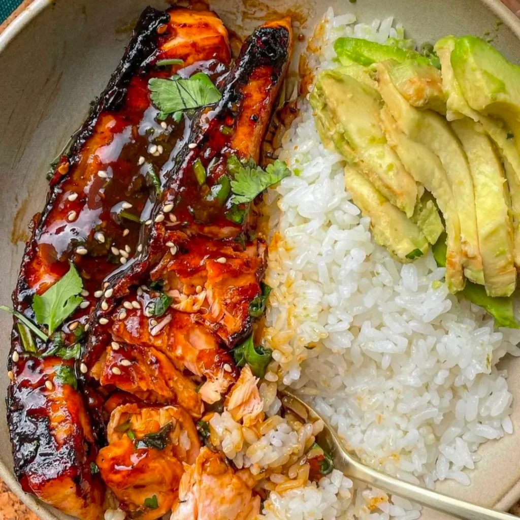 A serving plate with salmon, avocado , salsa and rice.