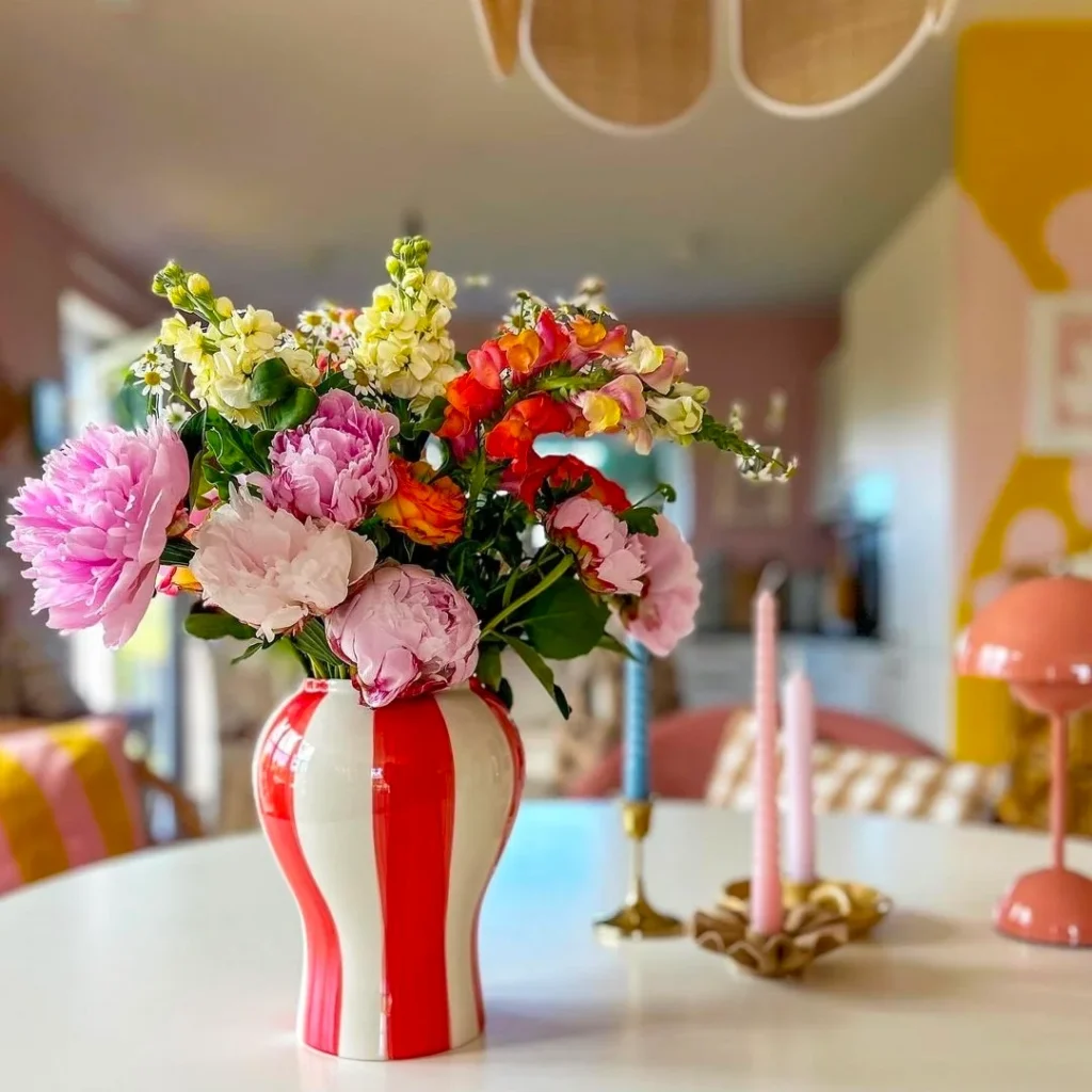 A beautiful red and white lined vintage vase is placed on the table. some vintage candle holders are also there.