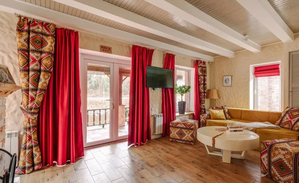 A spacious granny chic living room in brown and red color scheme is shown. red and brown heavy curtains are hanging on windows.