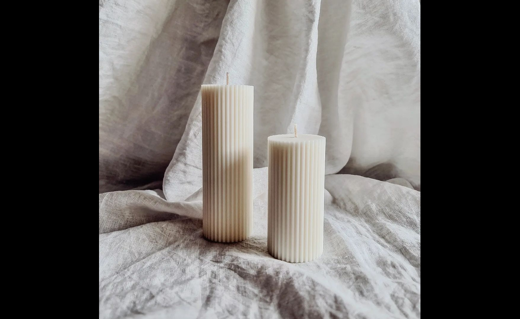 two white pillar candles placed on white bedding.