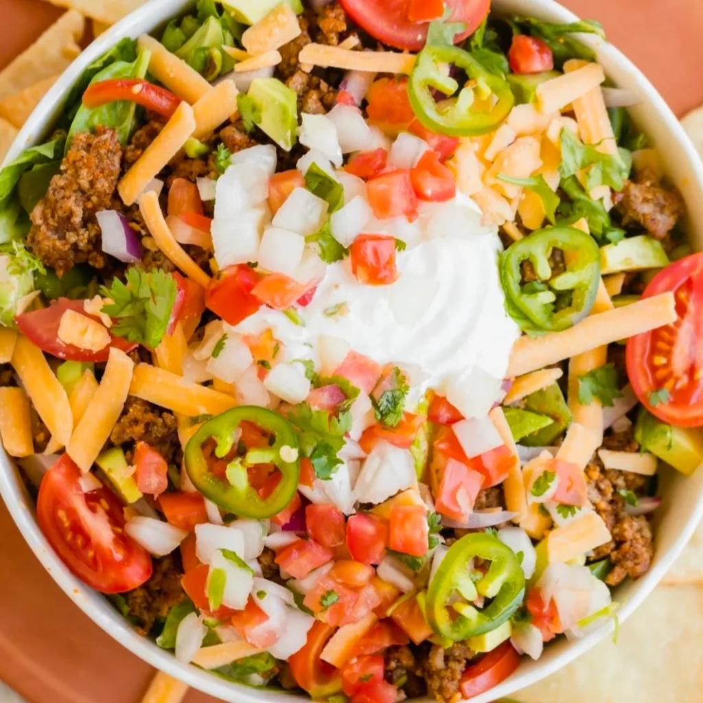 A big white bowl of taco salad with lots of green and red vegetables.