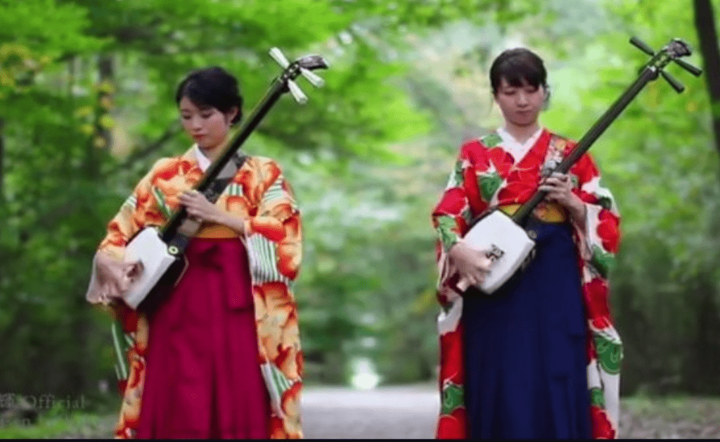 Two young japanese girls weraing traditional dresses and holding Japanese traditional musical instruments.