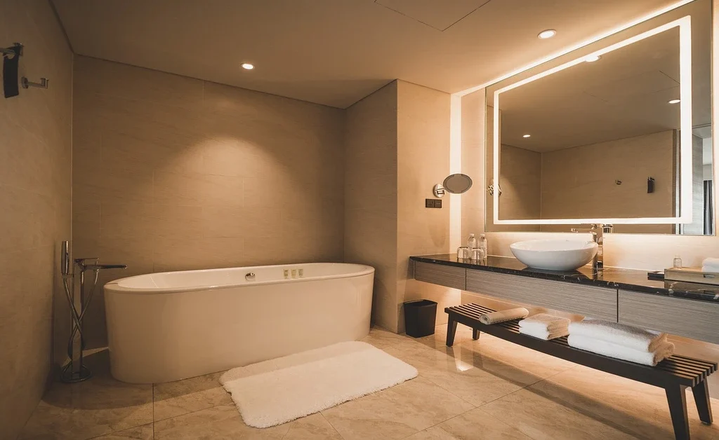 white freestanding bathtub, mirror placed over the sink bowls walls. folded towels placed on the wooden bench.