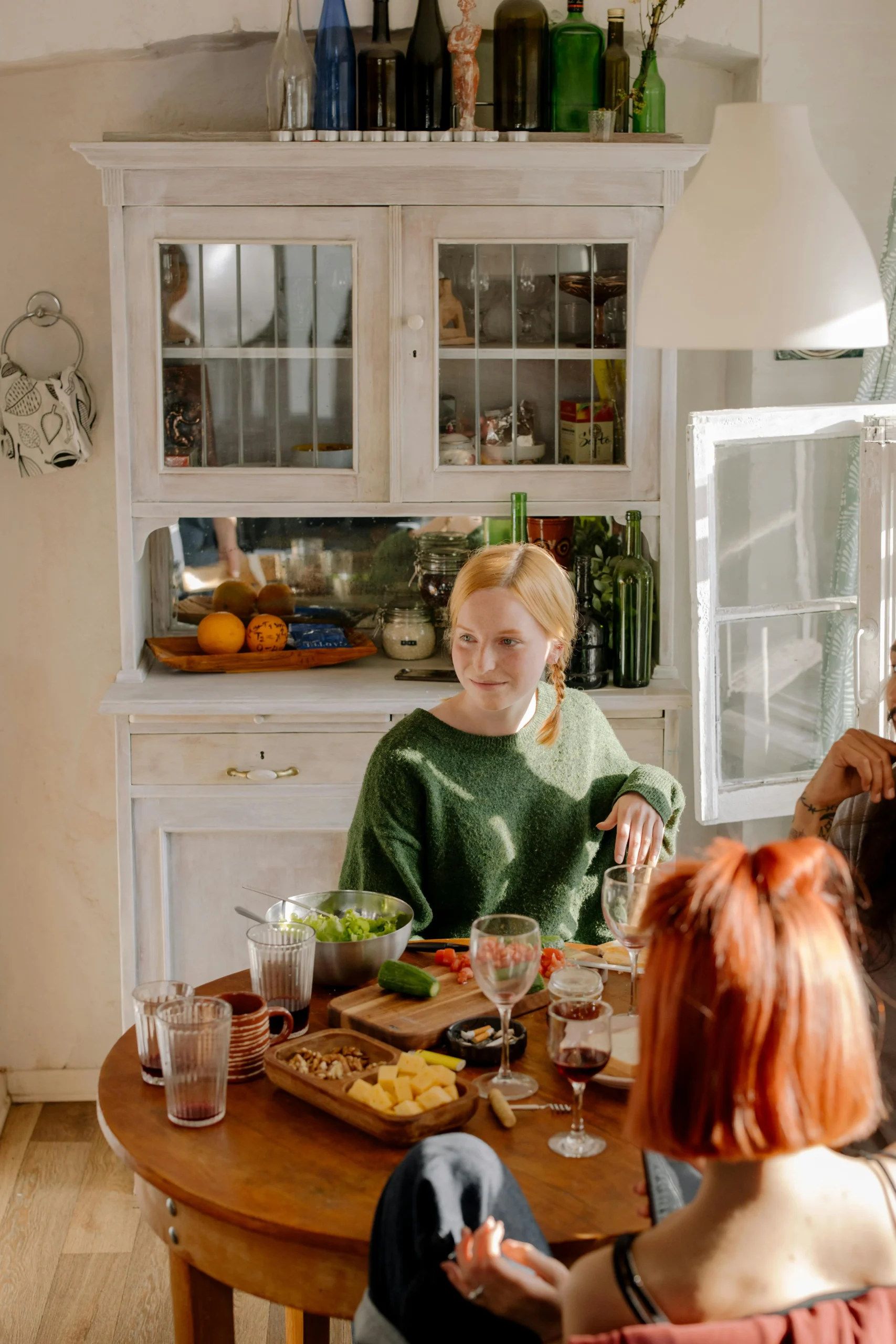 A girl in a green sweater is sitting in front of an open window. Behind her is an open shelf storage nook.