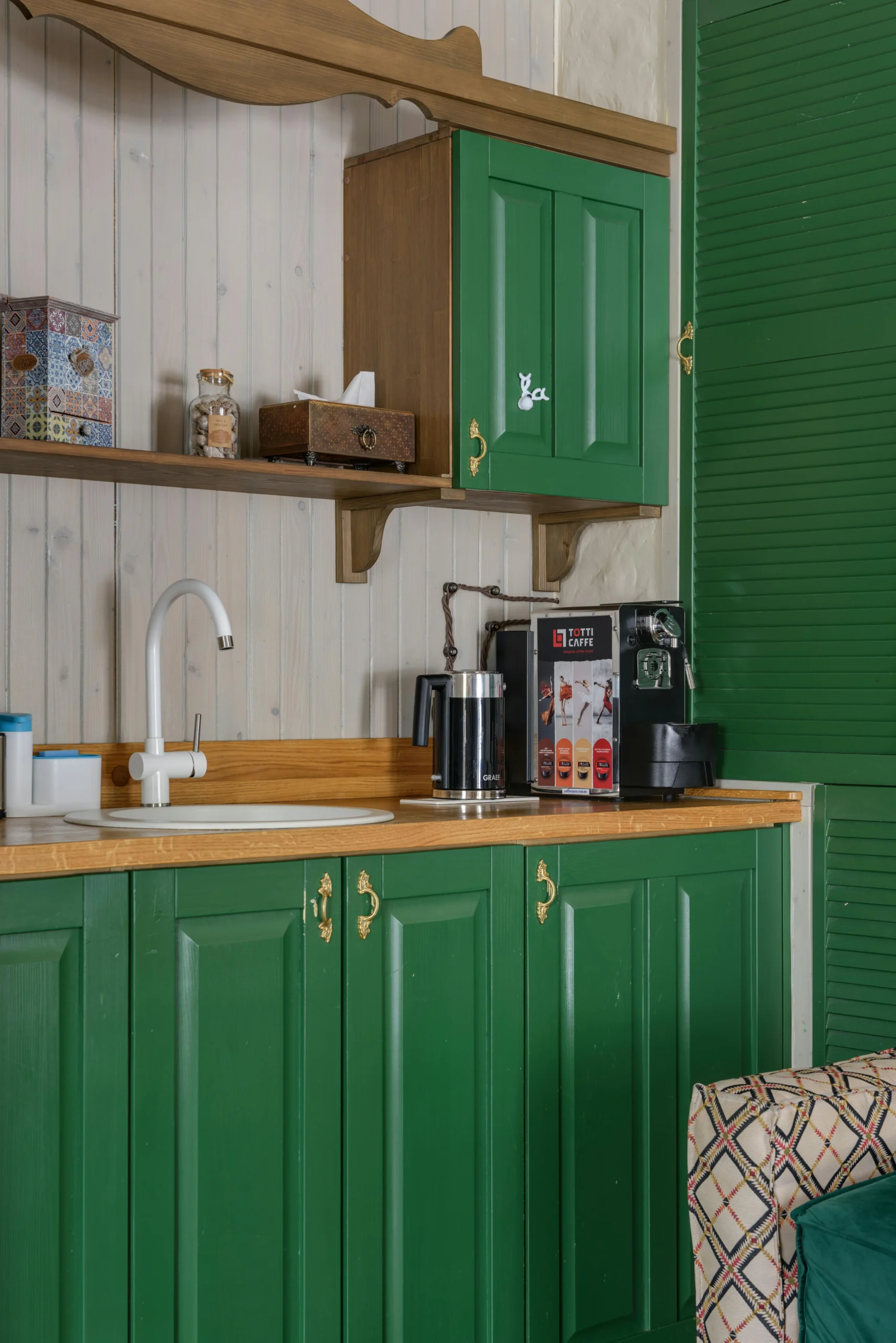 green below cabinets and green window on the right side of the white sink. above the sink is wooden cabinets for some storage.