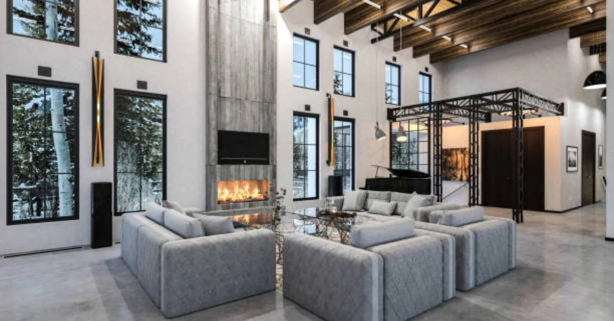 A soft grey toned open-layout industrial living room. grey sofas are on concrete floor. oversized bare windows on front.