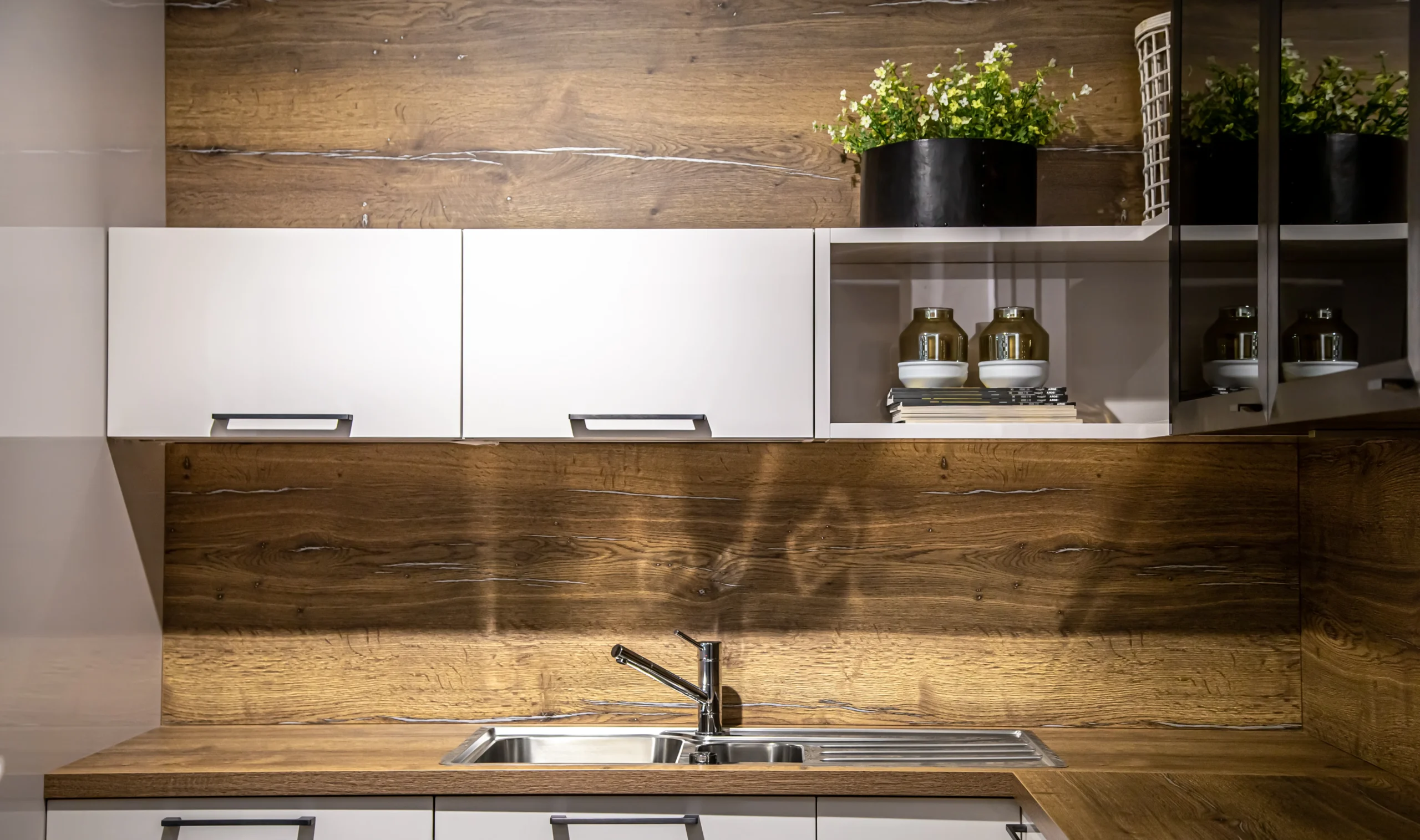 a black pot with plants placed above kitchen cabinets for decor. cabinets are white while the kitchen is wooden themed.